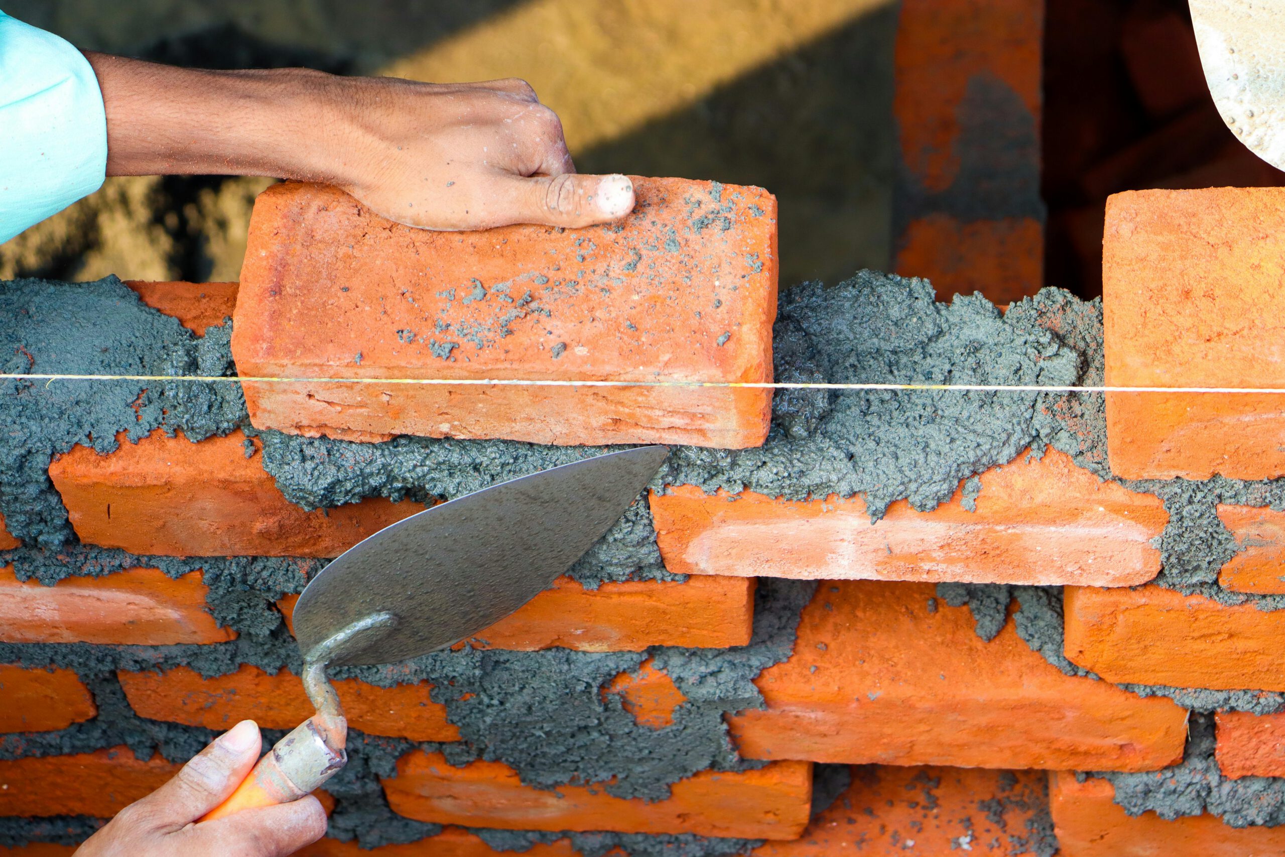 Home Hands laying bricks with cement in a construction setting, showcasing precise masonry work.